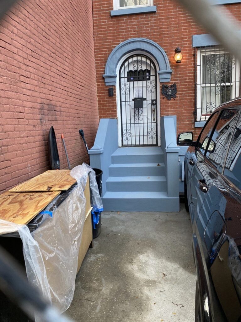 Finished gray-painted concrete stoop and steps at a brick home entrance with a black security door.